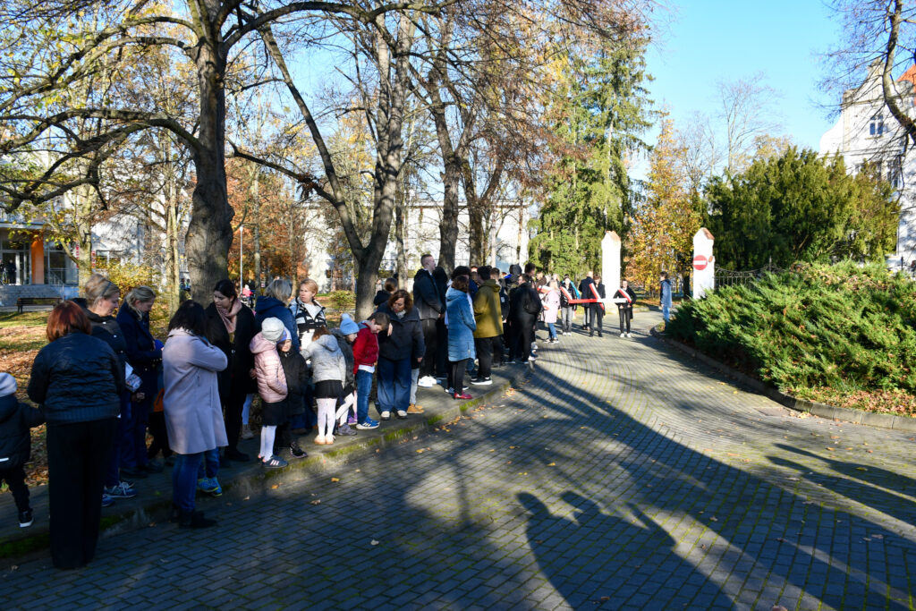 Grupa uczniów i nauczycieli stojących w parku podczas uroczystości patriotycznej.