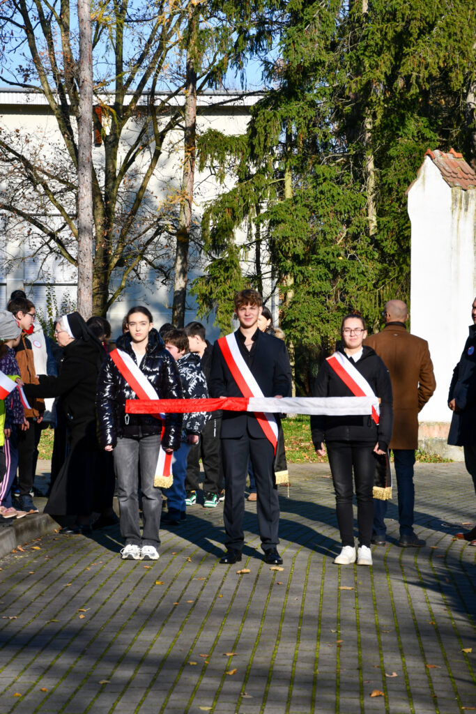 Poczet Sztandarowy w biało-czerwonych szarfach trzymający zwiniętą flagę podczas ceremonii.