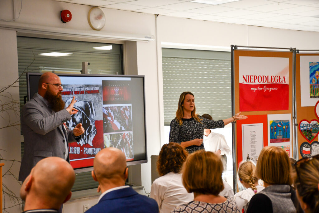 Prowadzący prezentujący slajd z materiałami historycznymi.