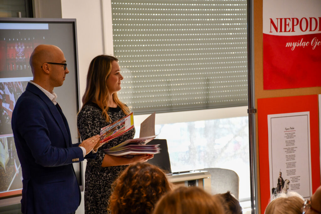 Dyrektor i nauczycielka odczytujący imiona i nazwiska uczniów wyróżnionych w konkursie.