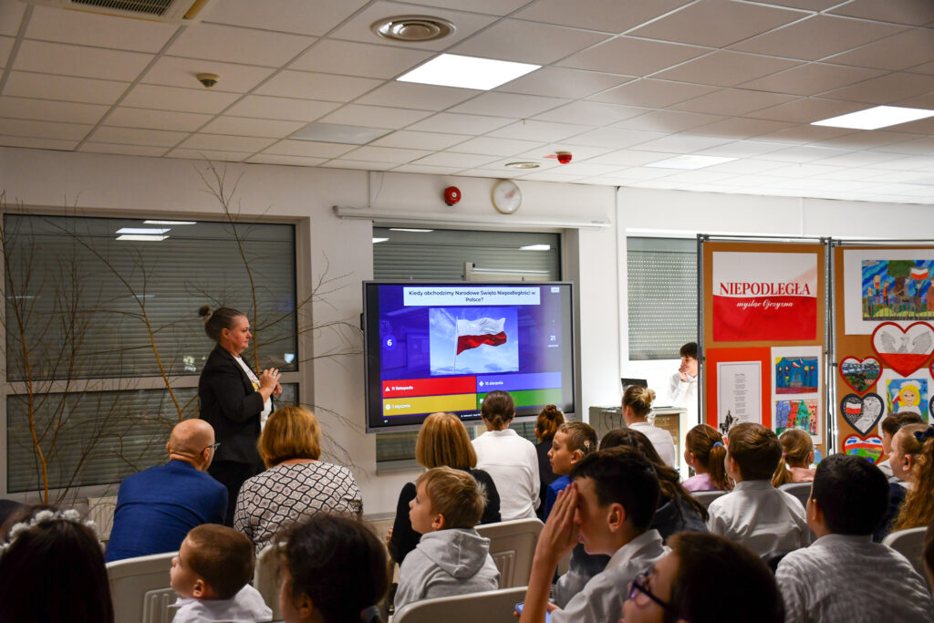 Prowadząca stojąca przy ekranie podczas prezentacji.