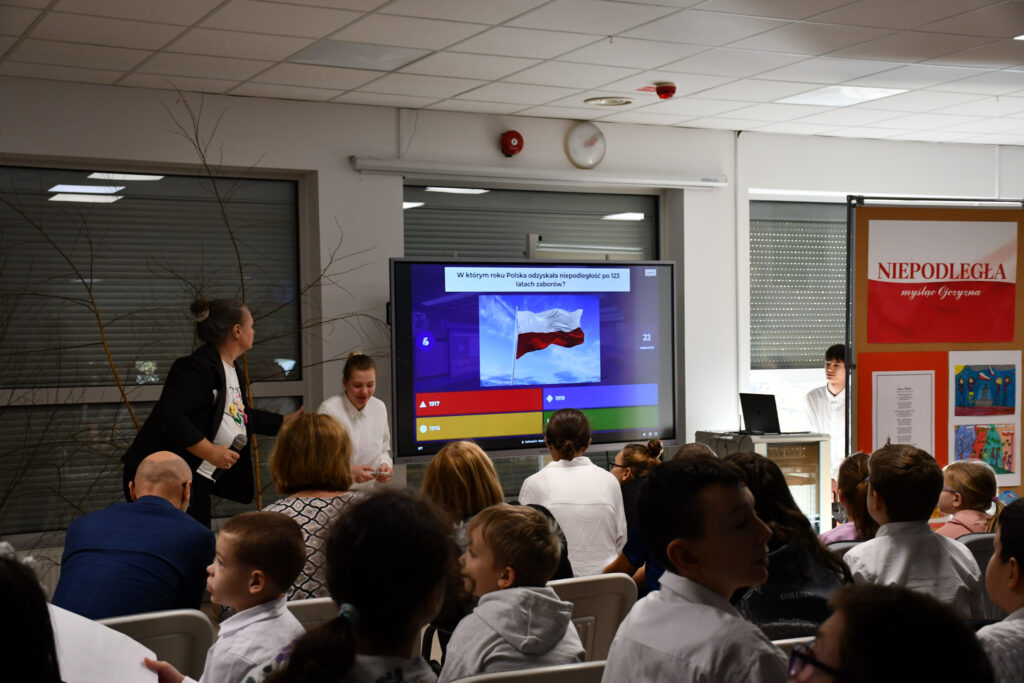 Prowadząca stojąca przy ekranie podczas prezentacji.