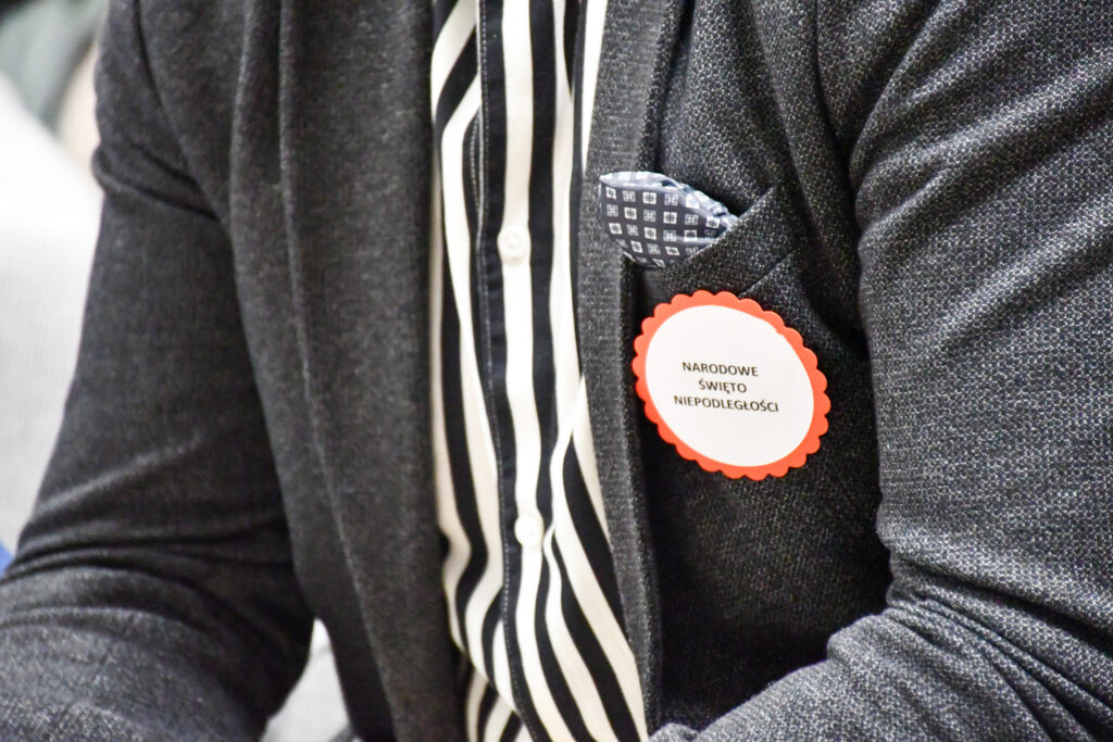 Detal przypinki z napisem patriotycznym przypiętej do marynarki.