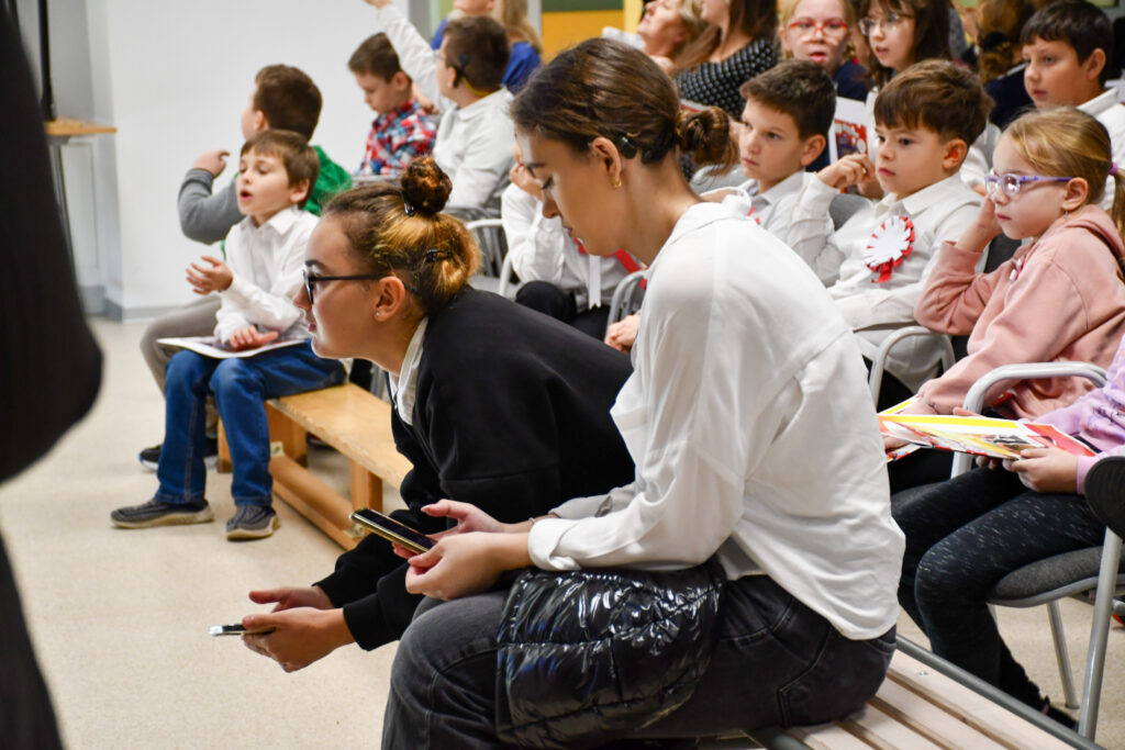 Uczniowie siedzący na widowni podczas szkolnego apelu.