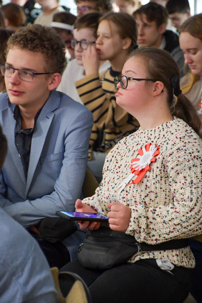 Grupa uczniów uważnie słuchających wystąpienia w sali.