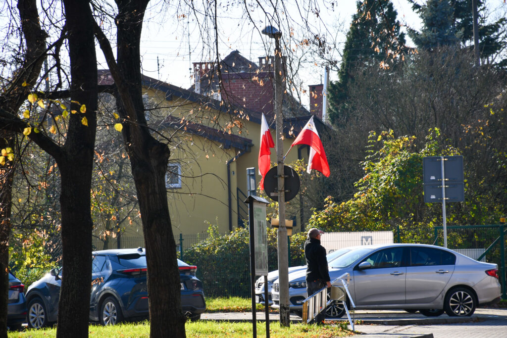 Flaga Polski powiewająca na tle budynków i drzew.