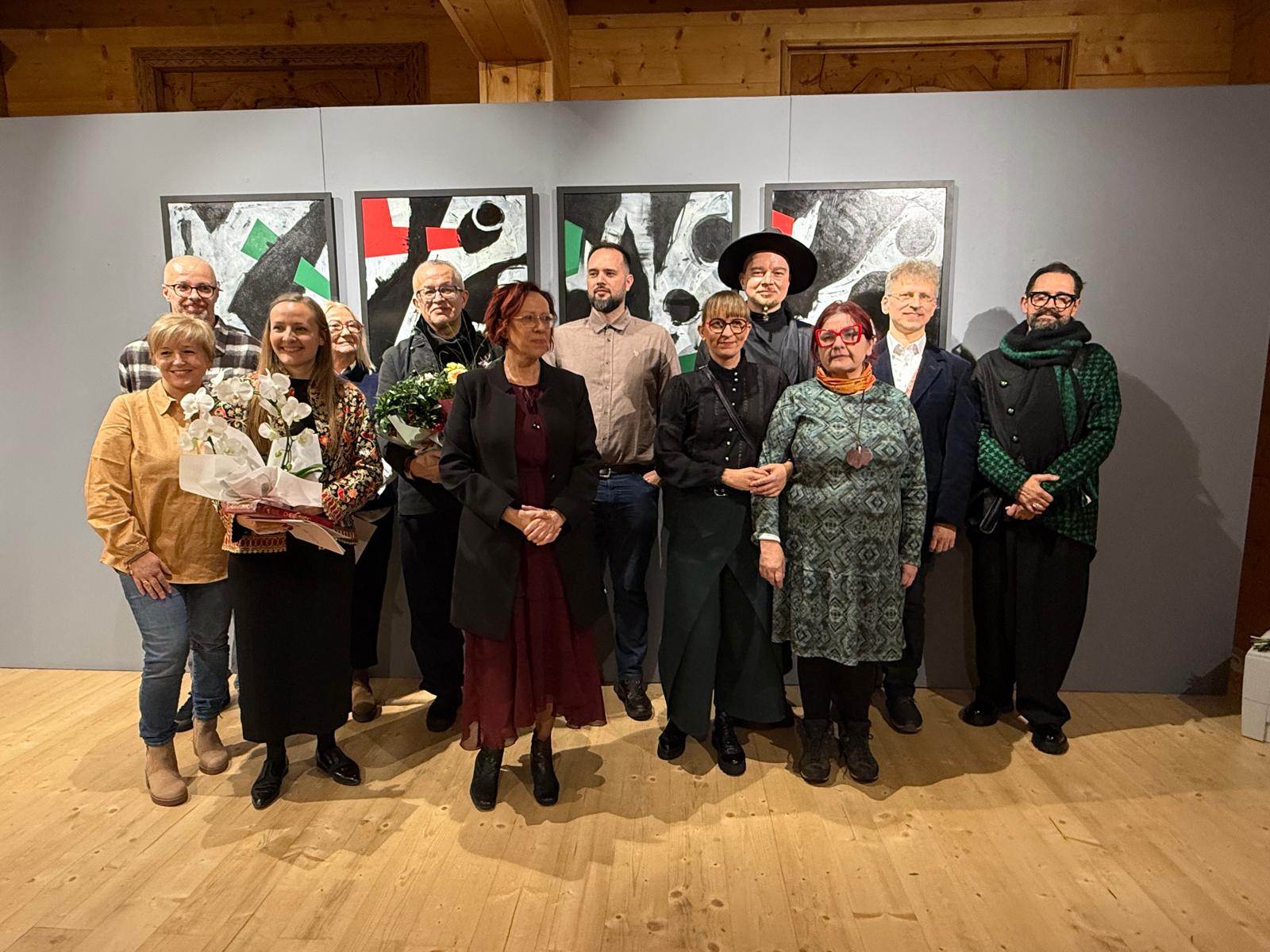 Grupa uczestników pozująca do wspólnego zdjęcia w sali wystawowej galerii.