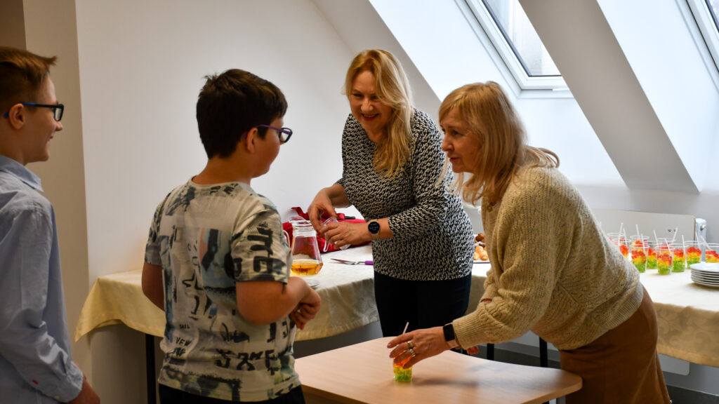 Nauczycielki częstują uczniów napojami i deserem.