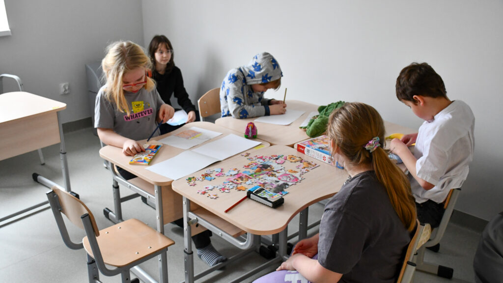Dzieci siedzą przy stole i rysują oraz układają puzzle podczas zajęć w świetlicy.