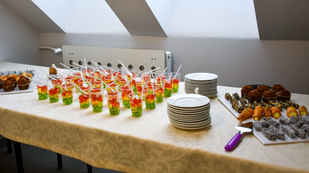 Stół z poczęstunkiem: kolorowe galaretki w kubkach, ciasta i talerzyki przygotowane dla uczniów.