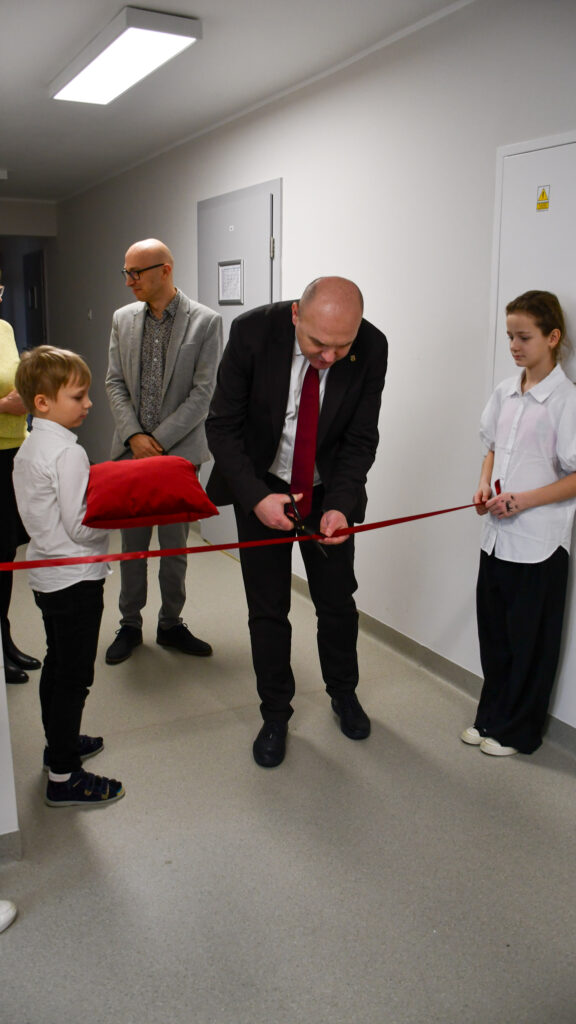 Mężczyzna przecina czerwoną wstęgę podczas szkolnej uroczystości otwarcia.