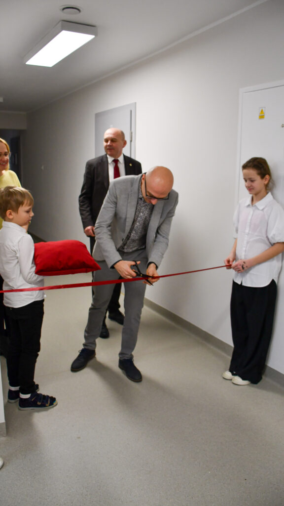 Drugi uczestnik ceremonii przecina czerwoną wstęgę w obecności uczniów.