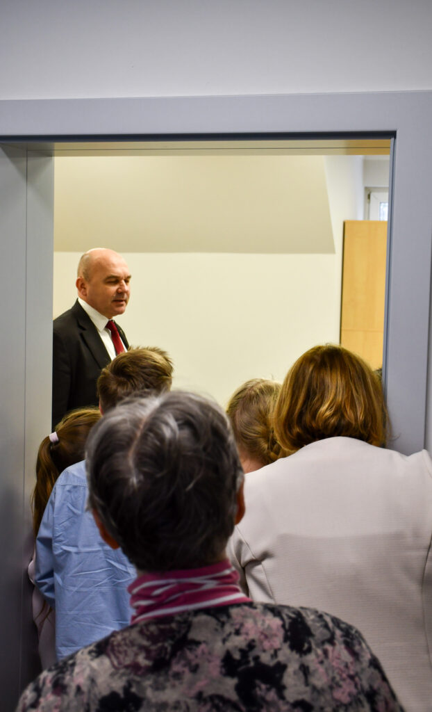 Grupa osób obserwuje przemówienie w drzwiach sali lekcyjnej.