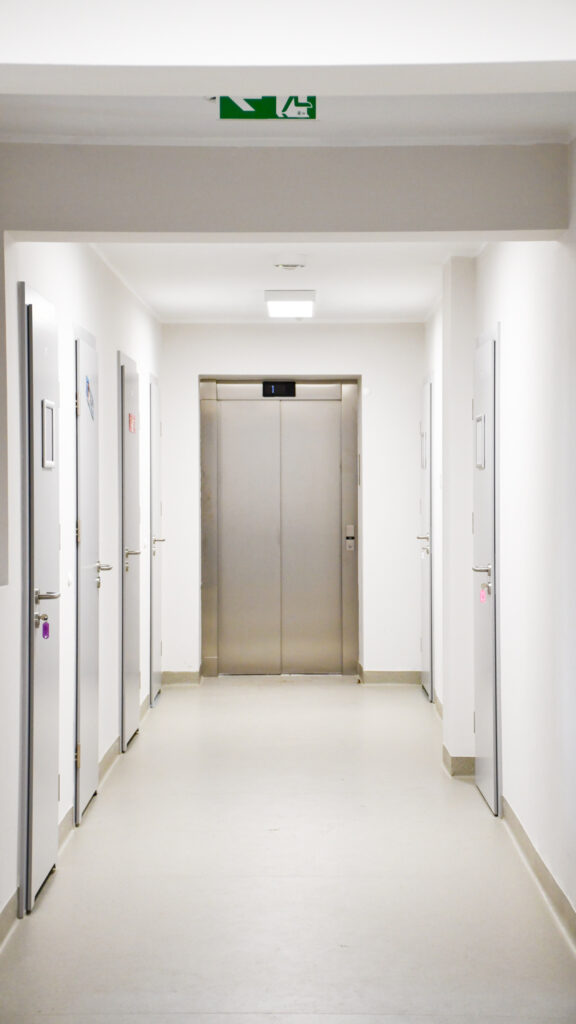 Szkolny korytarz z windą i oznaczeniem drogi ewakuacyjnej.