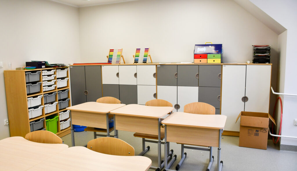 Sala lekcyjna z ławkami, szafkami i pomocami edukacyjnymi.