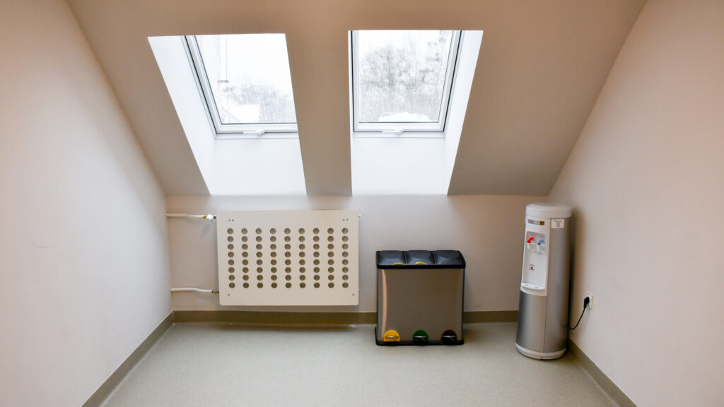 Kącik na korytarzu pod oknami dachowymi z pojemnikami do segregacji odpadów i dystrybutorem wody.