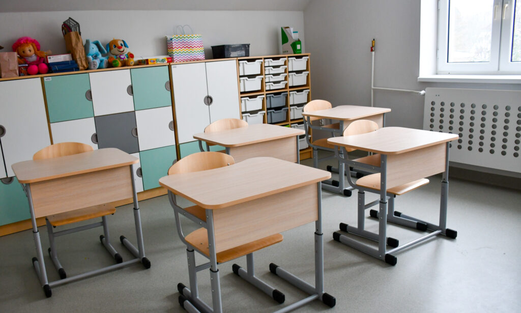 Sala lekcyjna z ławkami, szafkami i pomocami edukacyjnymi.